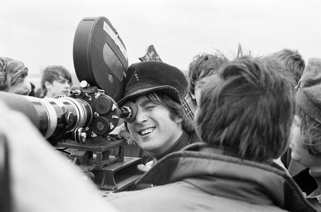 John Lennon looking through the lens of a camera during shooting