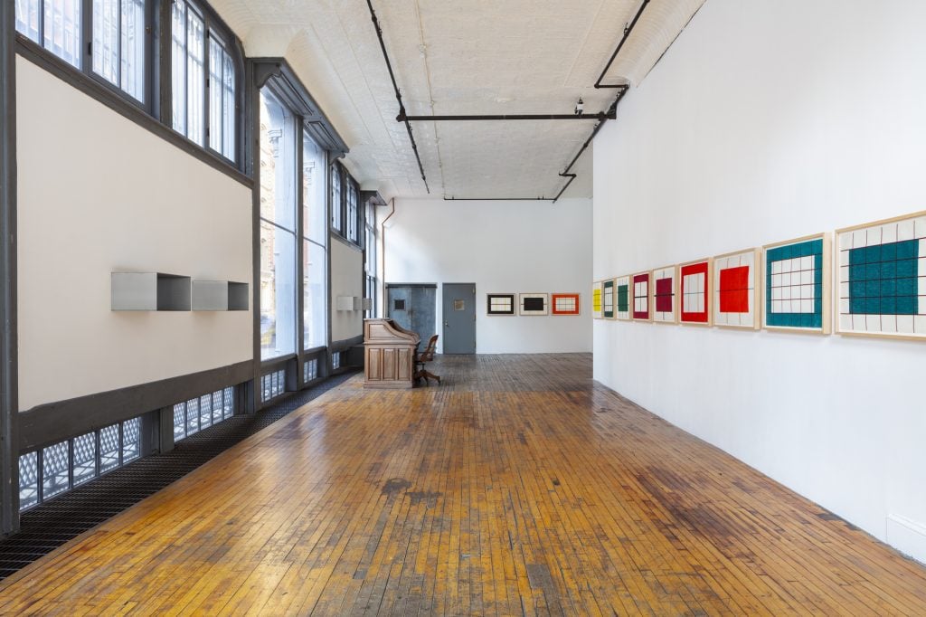 A photograph of an airy, almost empty industrial New York apartment lined with colorful geometric prints on the right wall