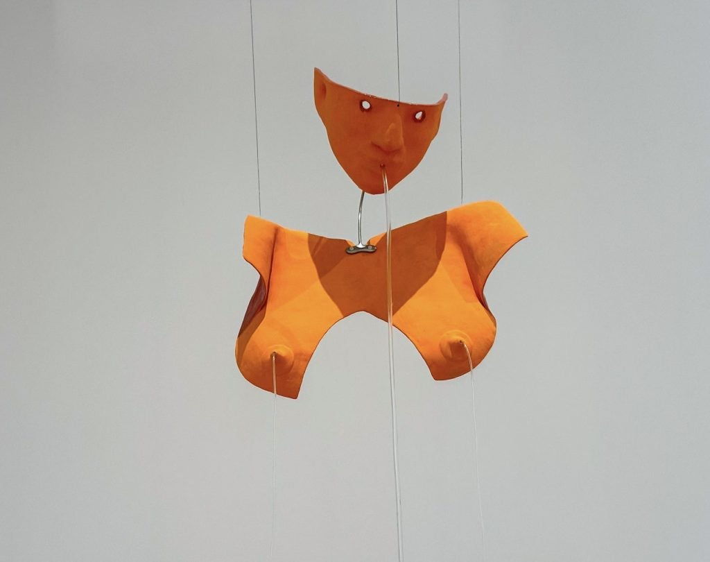 A sculpture of a suspended orange fragmented female body with tubes coming out of it