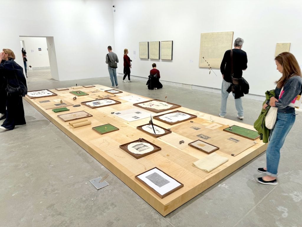 Various objects laid out in a display on the ground, with canvasses on the wall behind featuring abstract pages that resemble book pages
