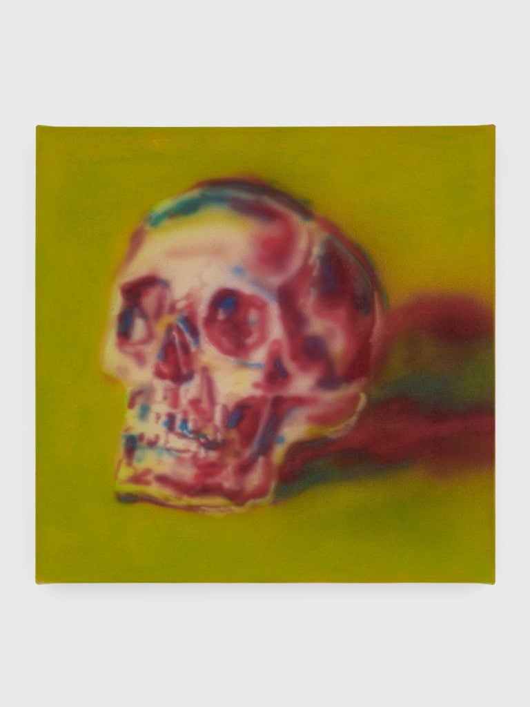 An pressure gun painted depiction by Katie Hector of a skull in multicolor against a grass green backdrop.