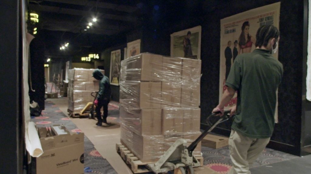Two men rolling pallets of boxes into a cinema.