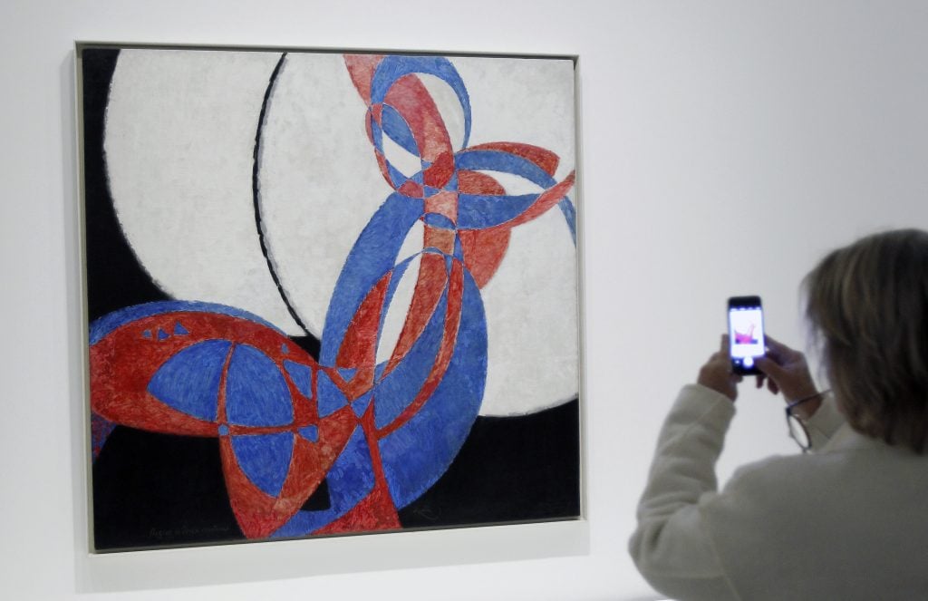An abstract canvas of intersecting blue and red forms displayed in a gallery