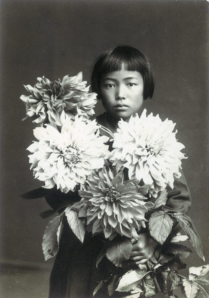An old black and white photograph of a ten year old Yayoi Kusama holding a huge blooming bouqet of flowers