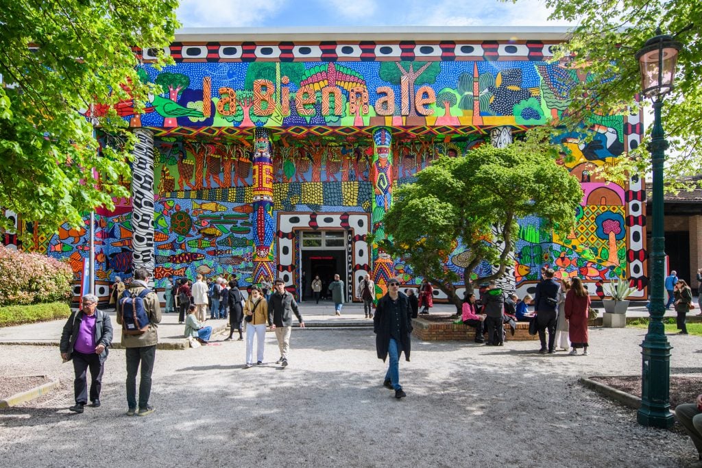 a crowd of people enter the colorful entrance of the venice biennale main pavilion