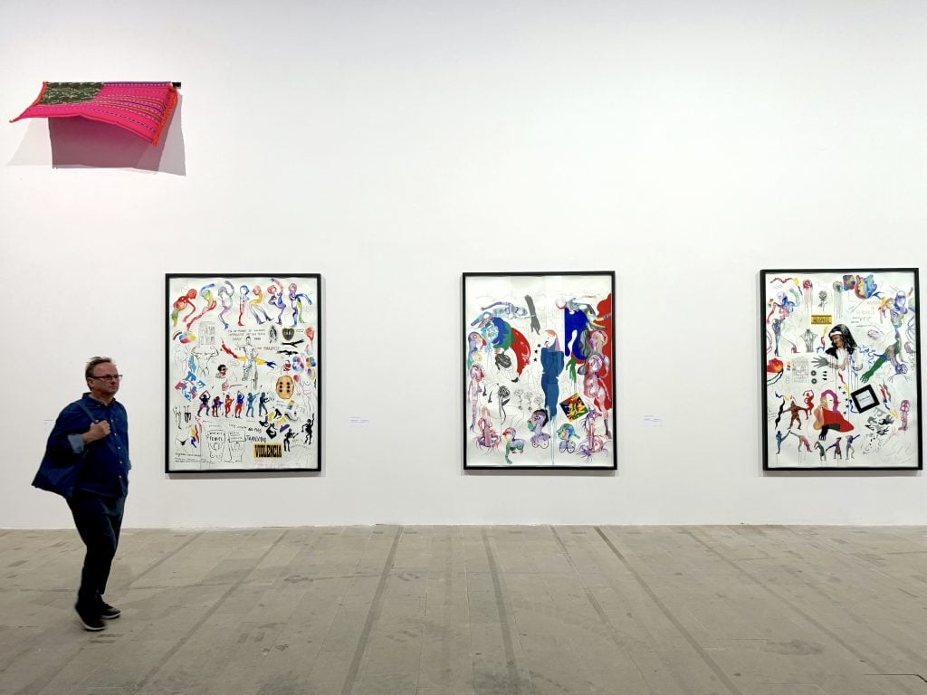 A man walks in front of three paintings and a flag hanging from the wall