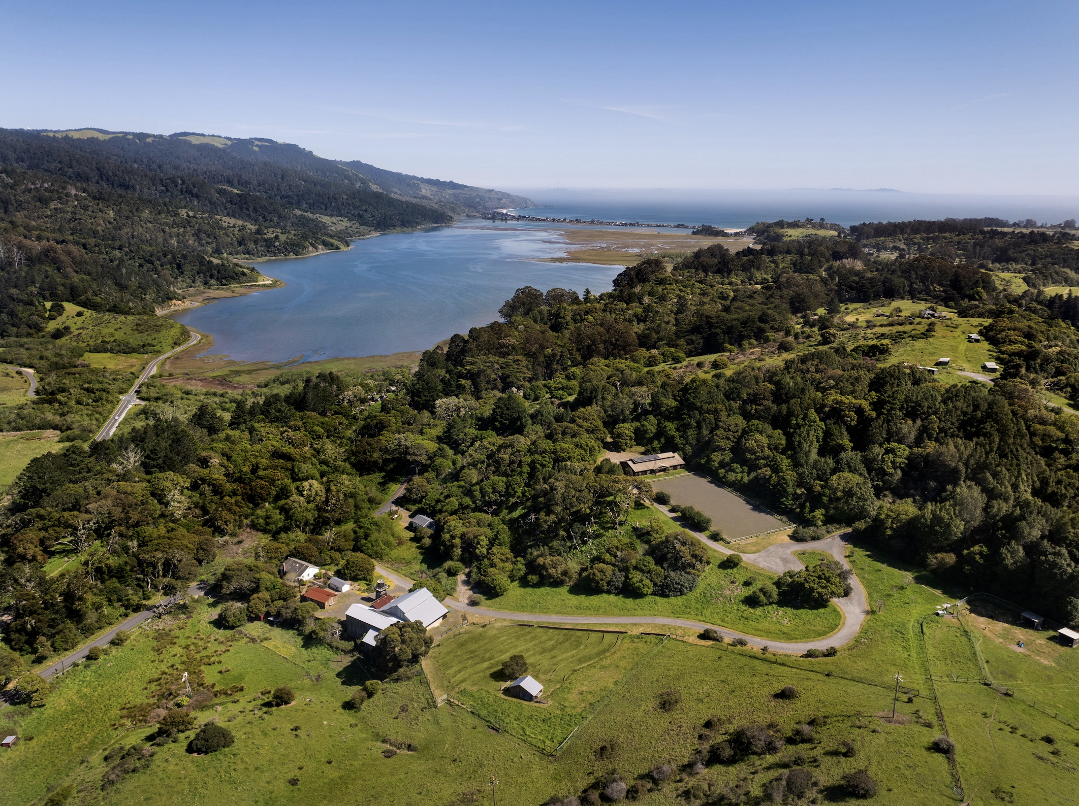 An aerial view of a farmhouse property owned by Annie Leibovitz and situated on greenery around a blue ocean cove