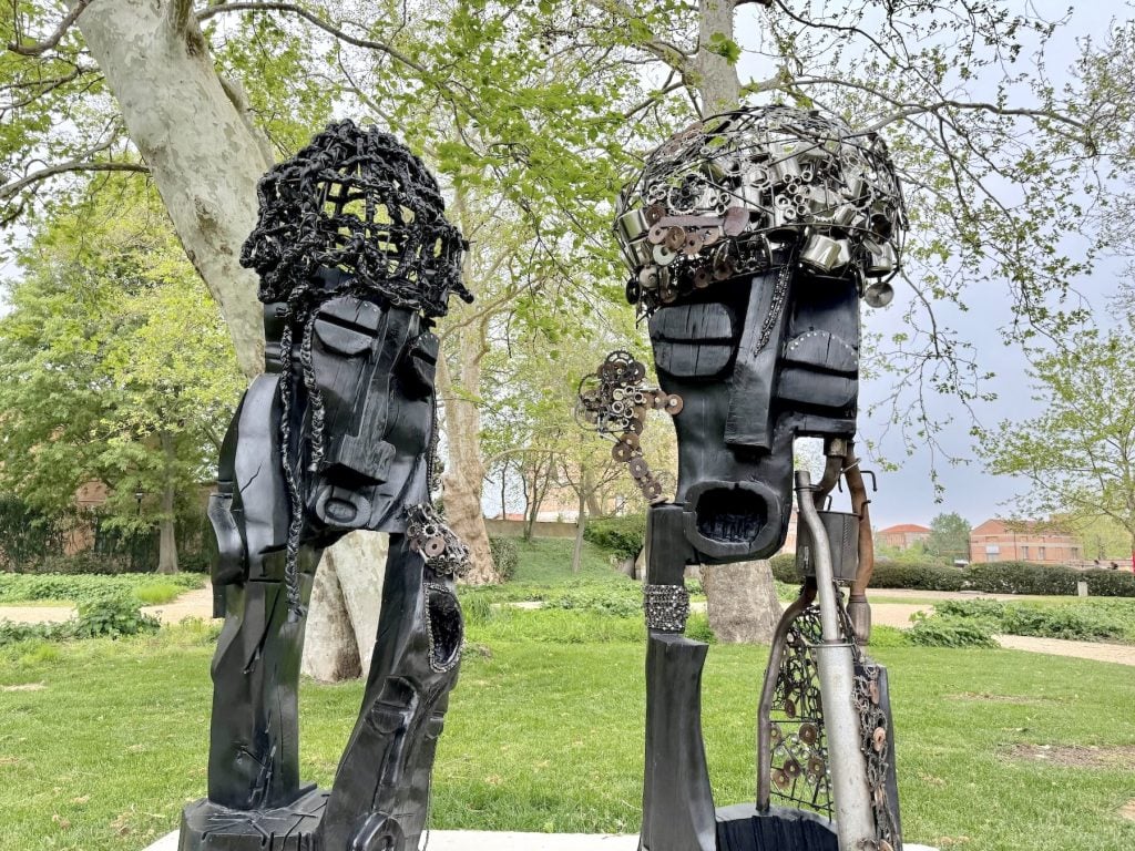 Two black sculptures of heads in a garden