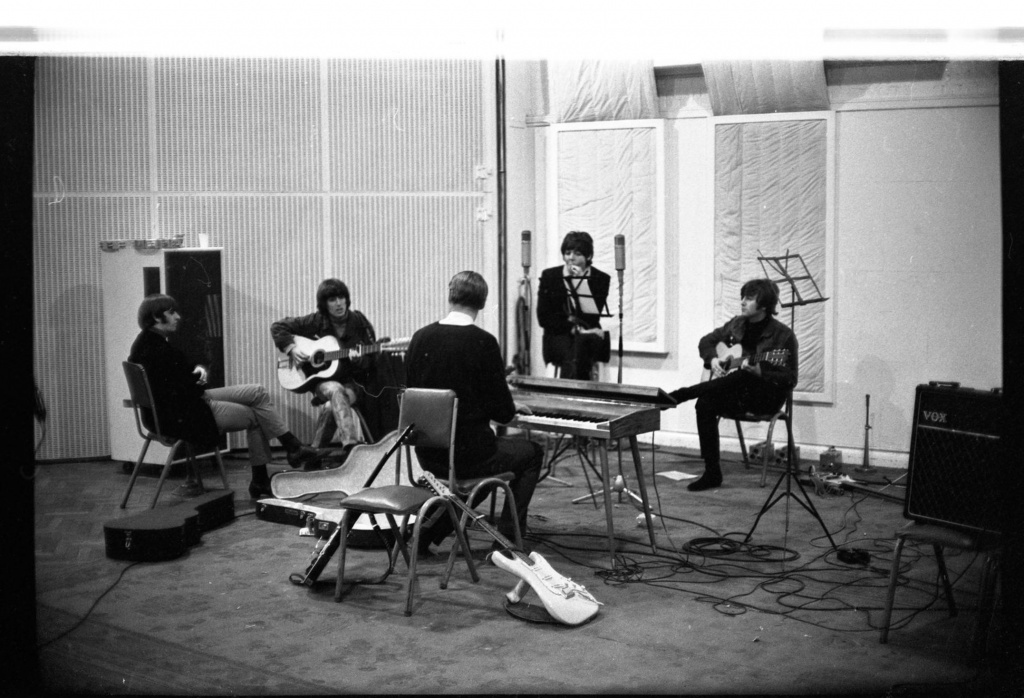 A black and white photo of the Beatles, with Lennon on the left, recording together in a sparse studio