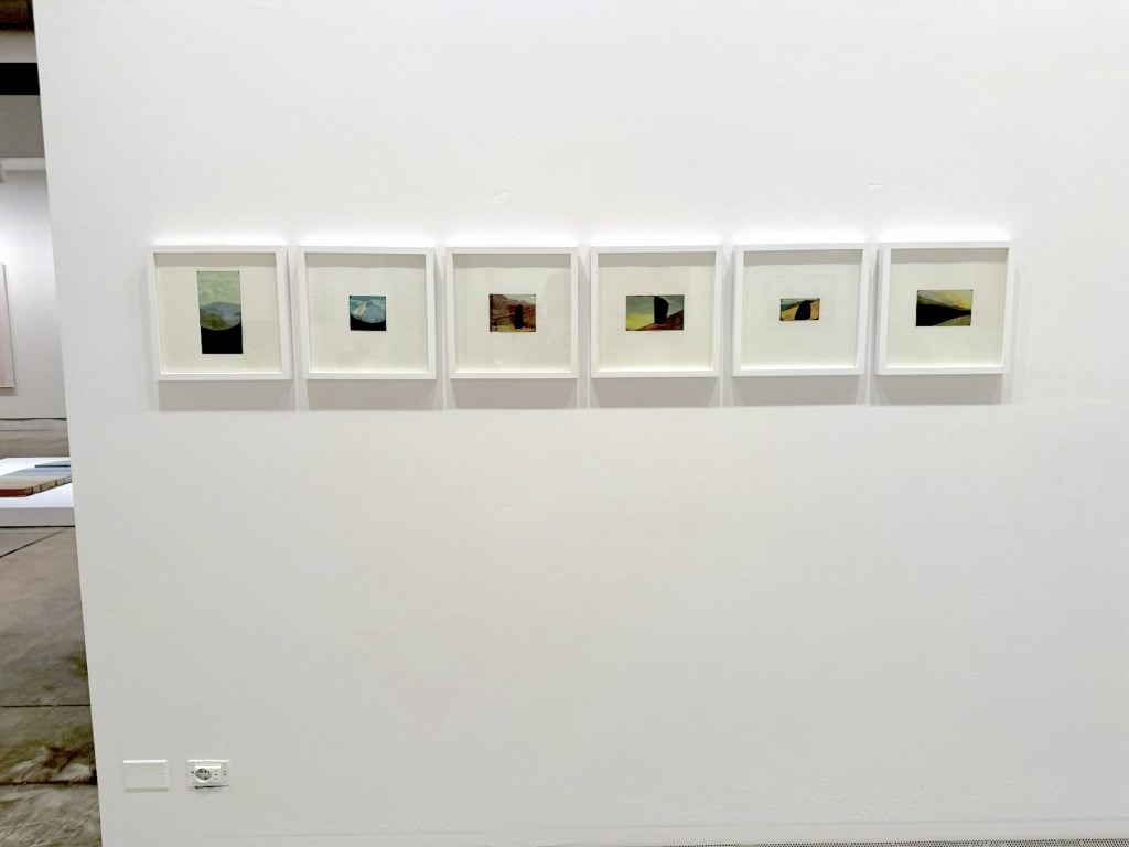 A row of small, mysterious landscapes displayed on a wall in a gallery