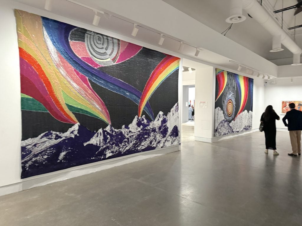 A gallery with two wall filling tapestries featuring mountains and rainbow imagery