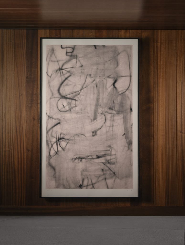 A large-scale silkscreen ink on paper in black and white, gestural and abstract, against a teak lined wall.