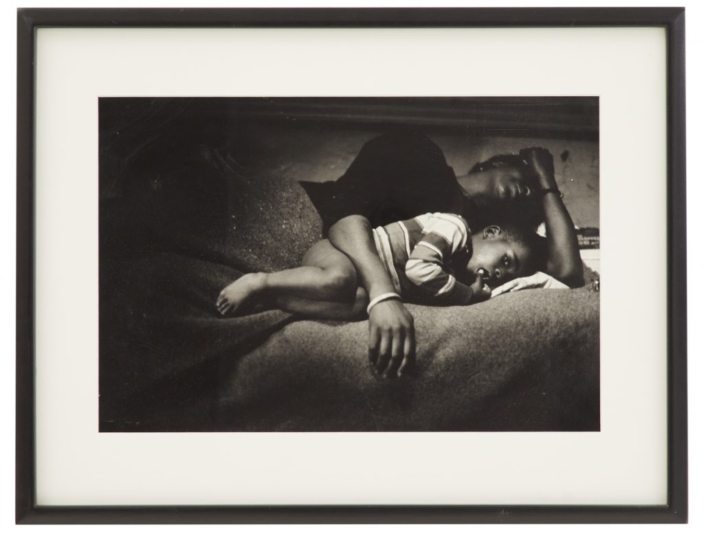 一名黑人妇女躺下，脸转过身，怀里抱着一个小男孩的黑白肖像。