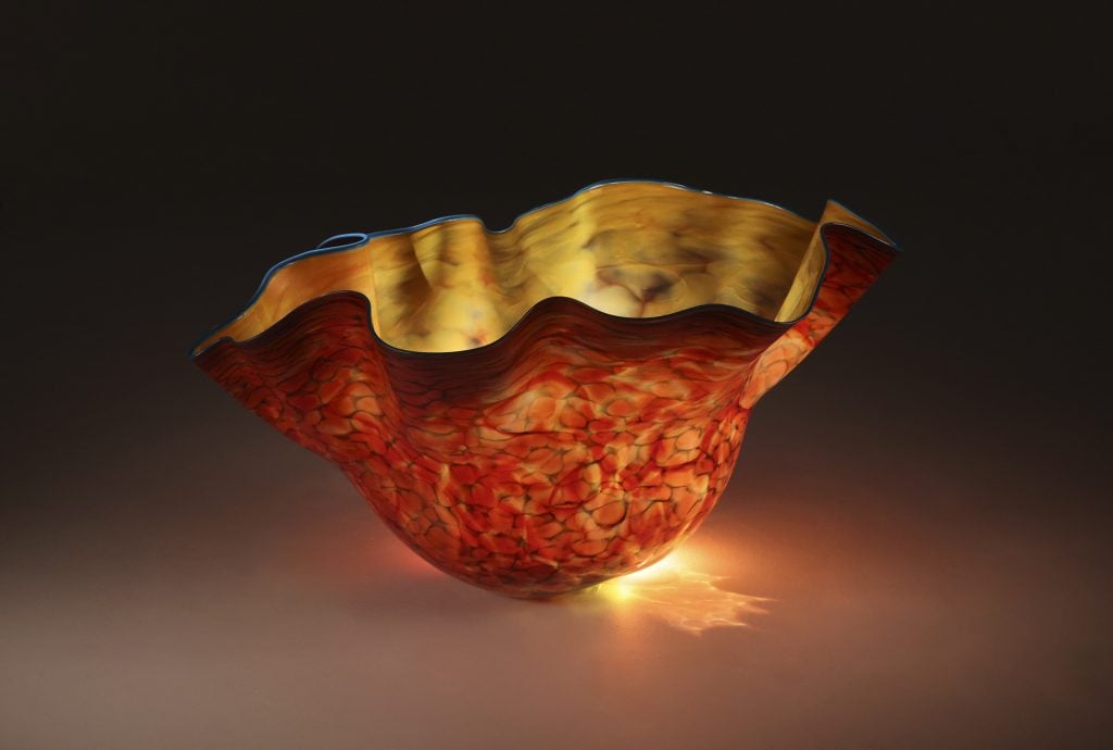 A large blown glass bowl organically shaped with a light in its center making it seem to glow.