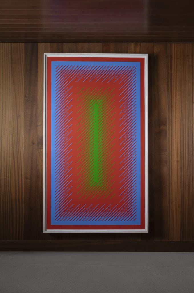 A rectangular abstract painting in portrait orientation with purple red and green on a teak paneled wall.