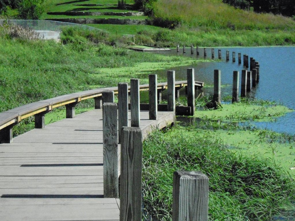 A land art installation in a park, featuring a boardwalk flanked with wooden structures.
