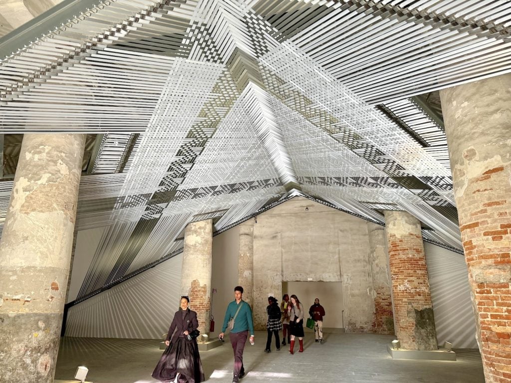 People walk beneath a giant canopy made of woven silver straps