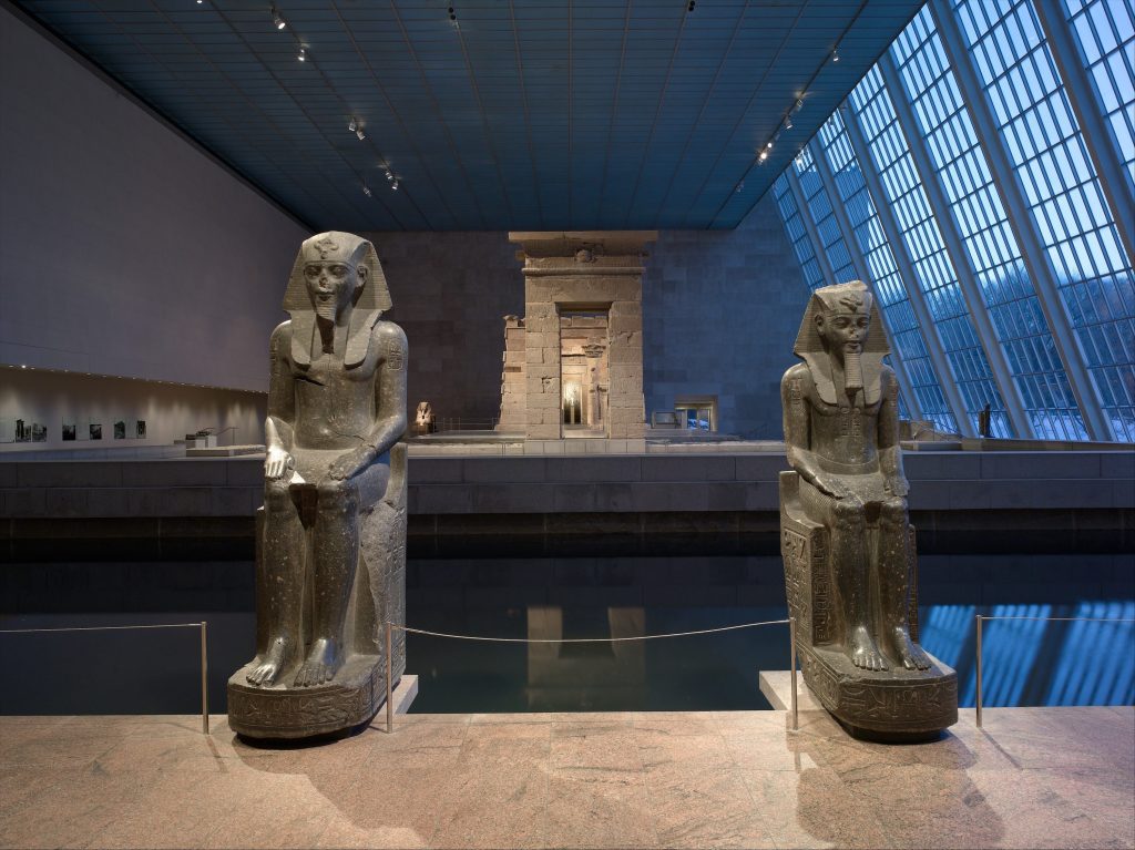 a view of the Temple of Dendur through two Egyptian statues