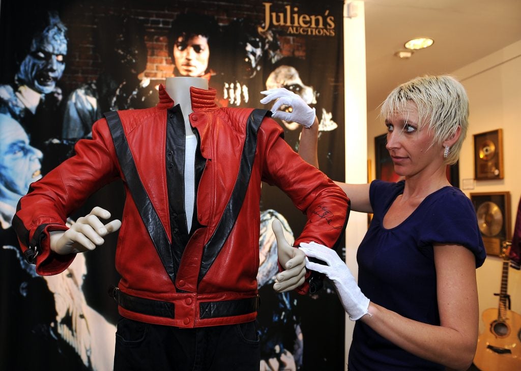 A woman adjusting a red jacket on a mannequin.