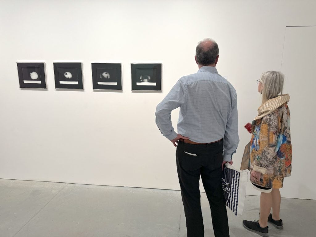 Two people observe a wall of four black and white photos in a gallery