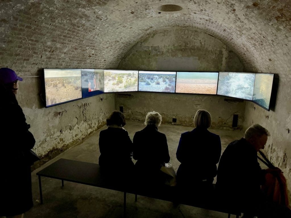 People watch a six-channel film of different barren landscapes in a cave