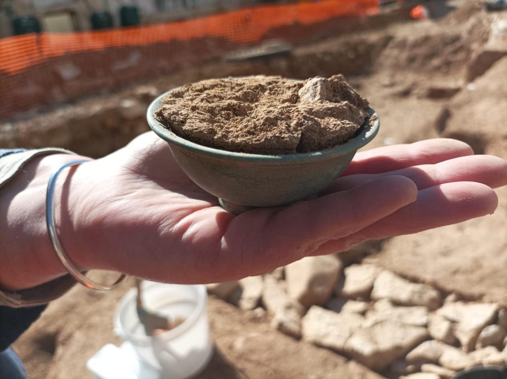 Glass cup filled with earth, held by hand.
