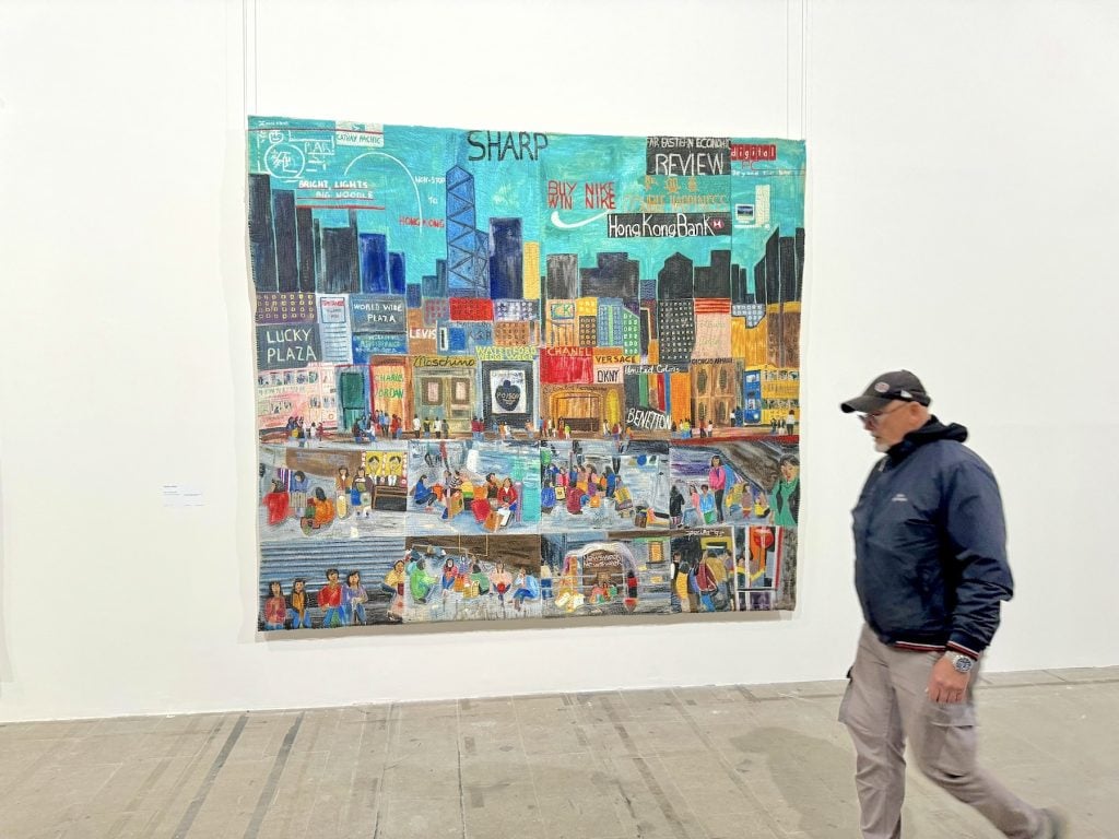 A man walks past a painting of a patchwork cityscape