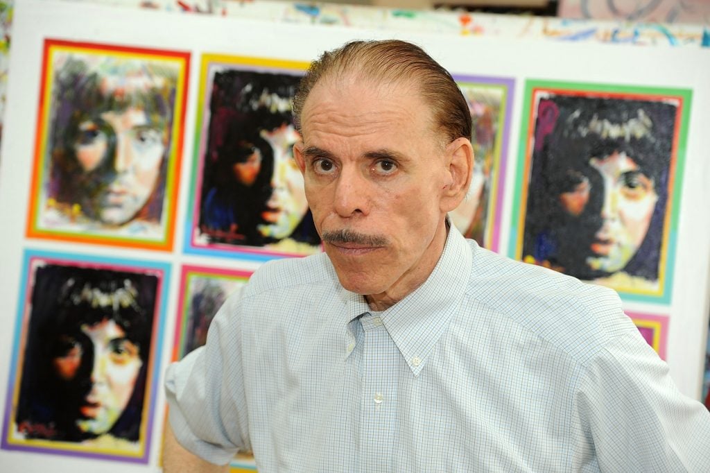 A man with a mustache, artist Peter Max, stands in front of paintings of Paul McCartney
