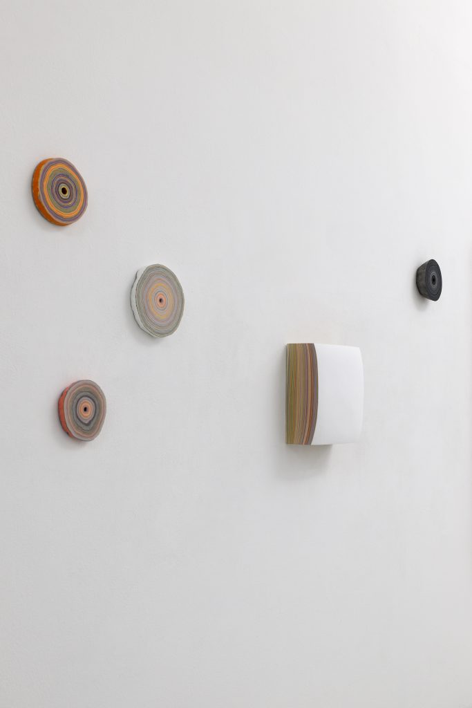 Four circular and one square petite ceramic pieces mounted on a white wall.