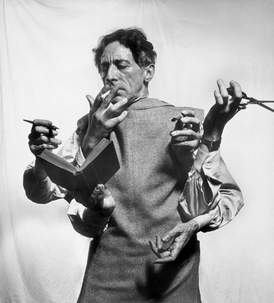 Surreal black and white photocollage depicting French poet and filmmaker Jean Cocteau with six arms performing different acts such as reading a book, holding a pen or a pair of scissors, and bringing a cigarette to his lips.