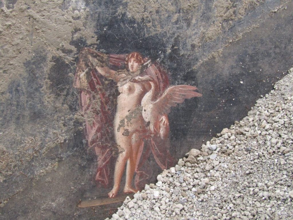 Ancient Pompeiian mural of a nude woman holding a red cape, a swan at her side.