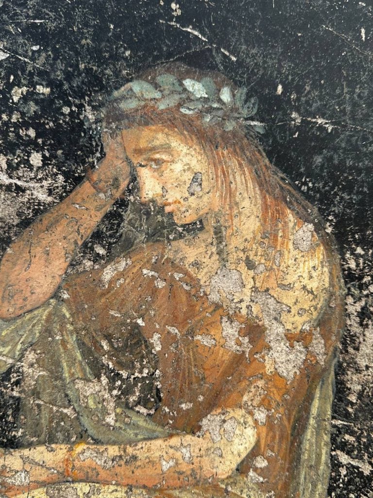 Close up of an ancient Pompeiian mural, showing a woman with a crown of leaves