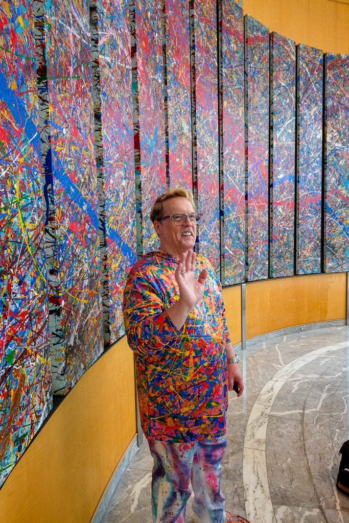 Portrait of Jumper Maybach standing in front of his multi-panel abstract painting.