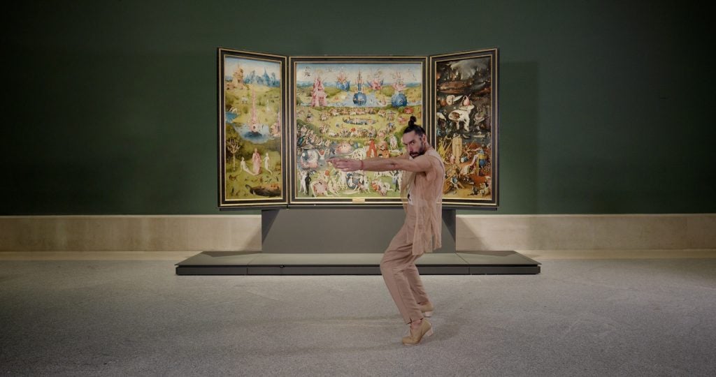 A dancer performs in front of a large painting by Hieronymous Bosch.