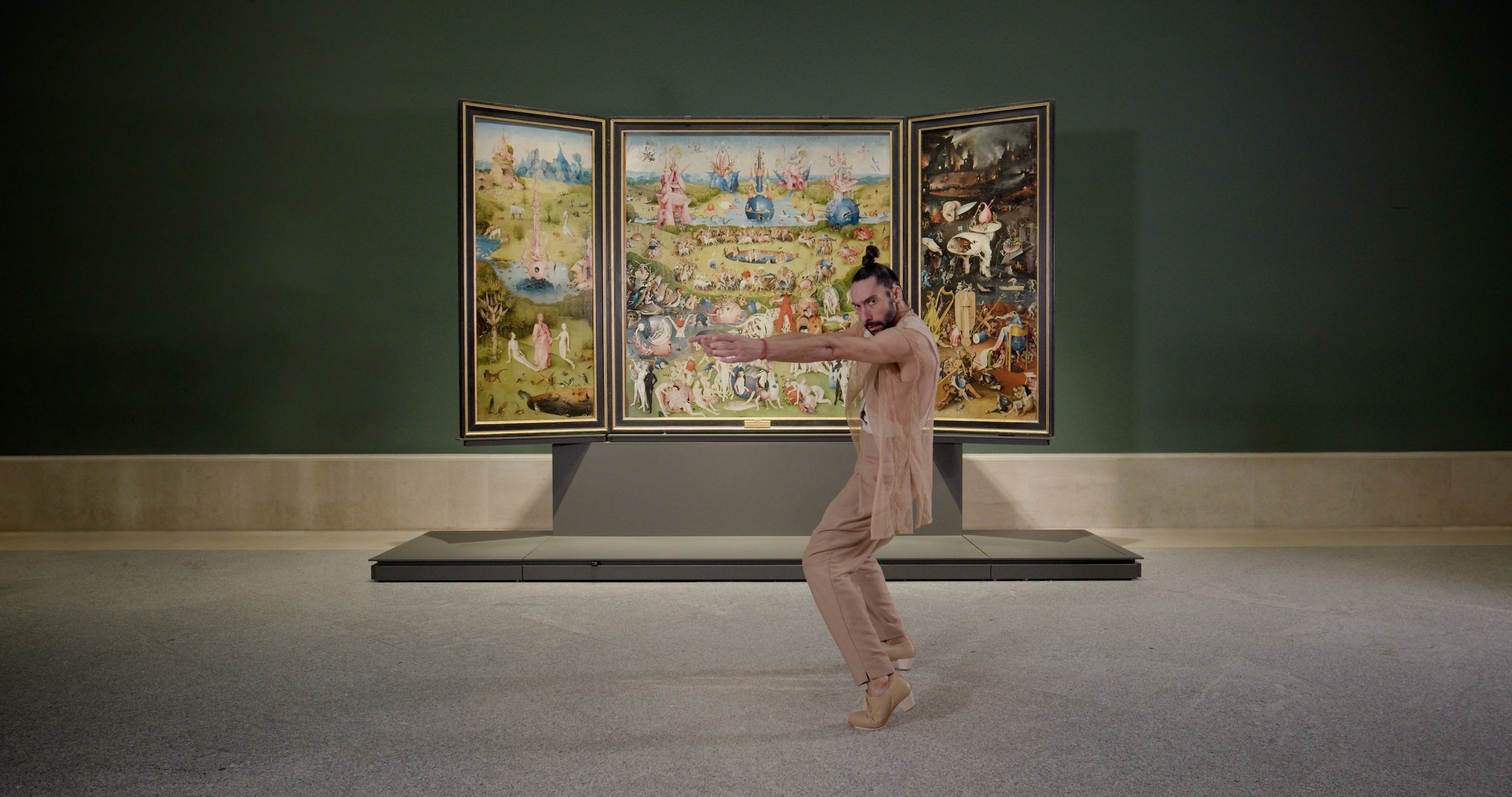 A dancer performs in front of a large painting by Hieronymous Bosch.