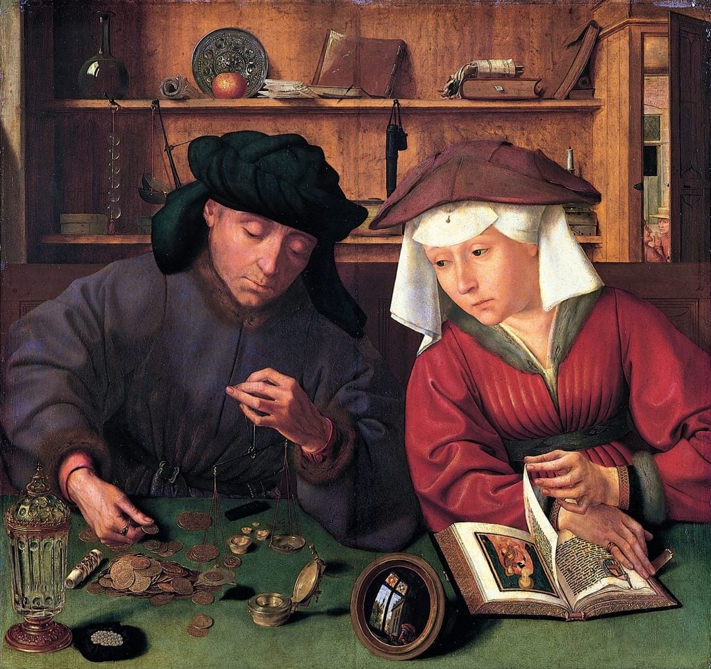 A man weighs jewelry and gold objects as his wife reads a prayer book