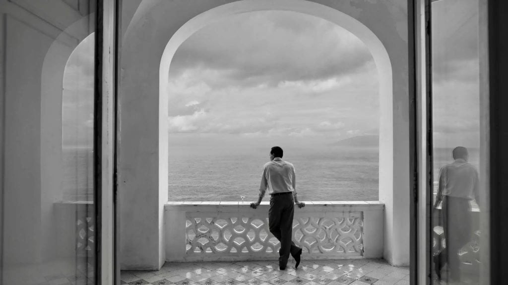 A man standing at a balcony viewing a vast sky.