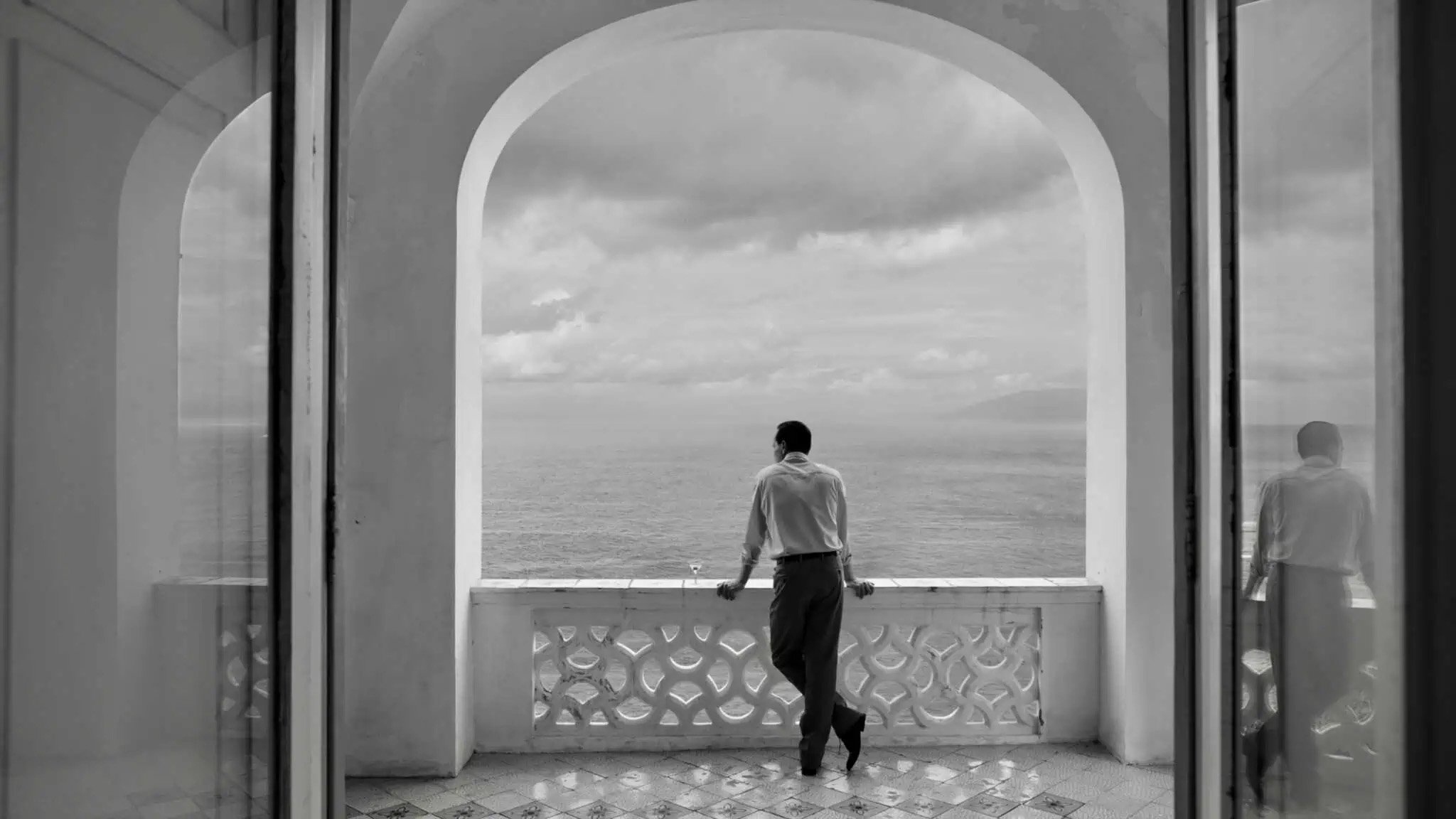 A man standing at a balcony viewing a vast sky.