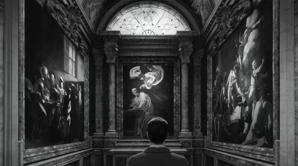 A man standing in front of three Caravaggio paintings depicting biblical scenes.