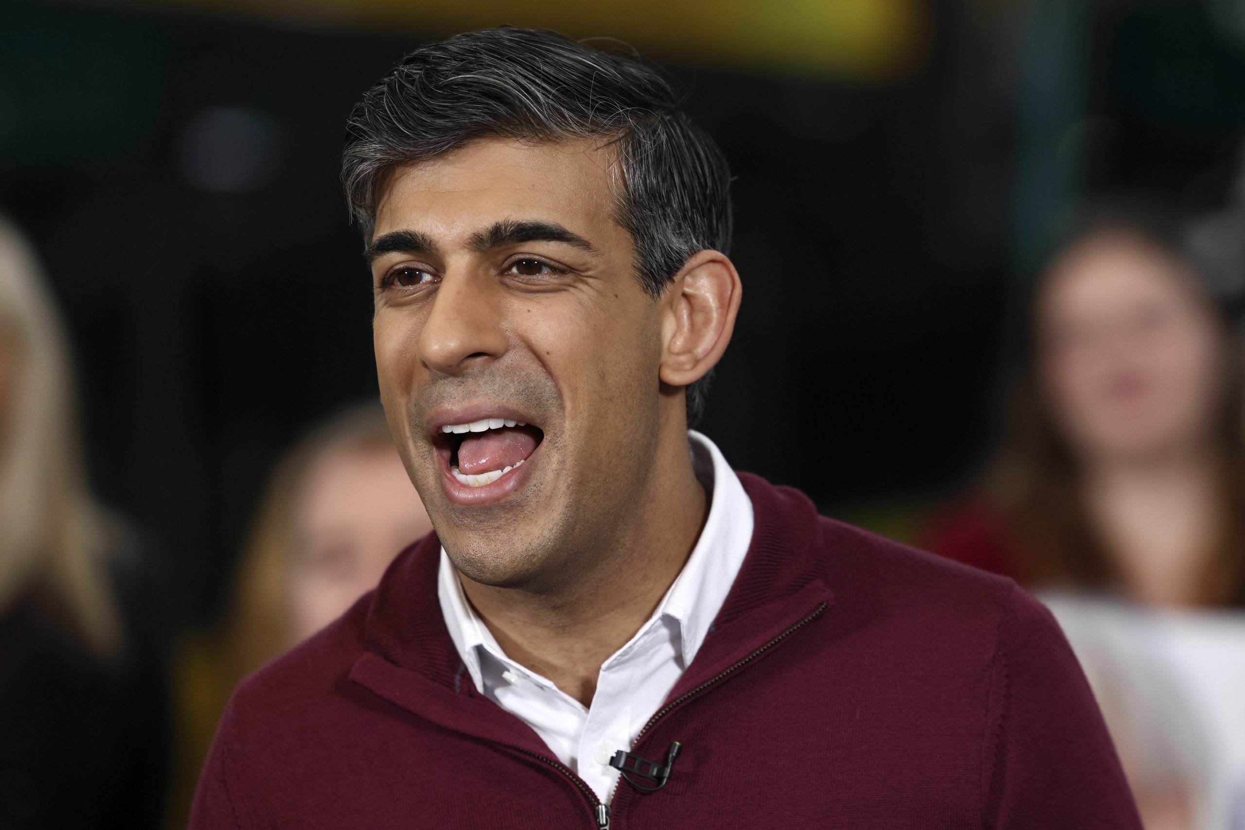 a smartly dressed man wearing a maroon jersey appears to be mid speaking