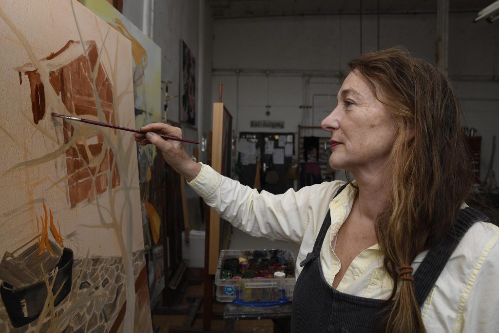 a middle-aged white woman with long auburn hair paints a canvas
