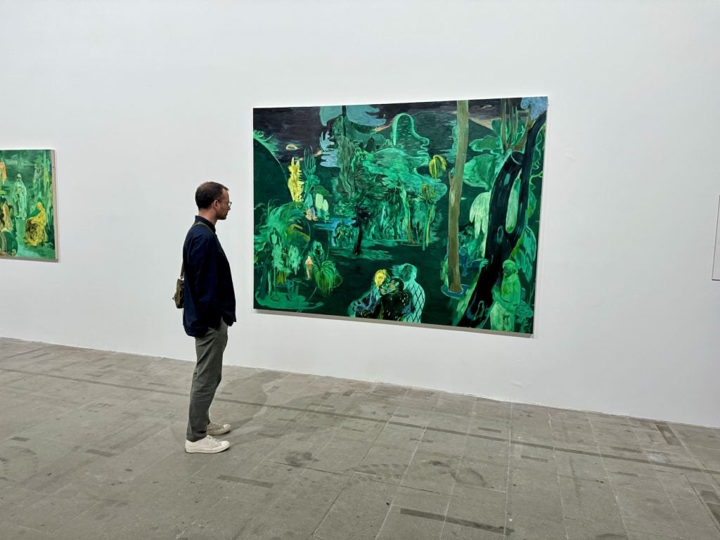 A man looks at a green-toned figurative painting of a grove