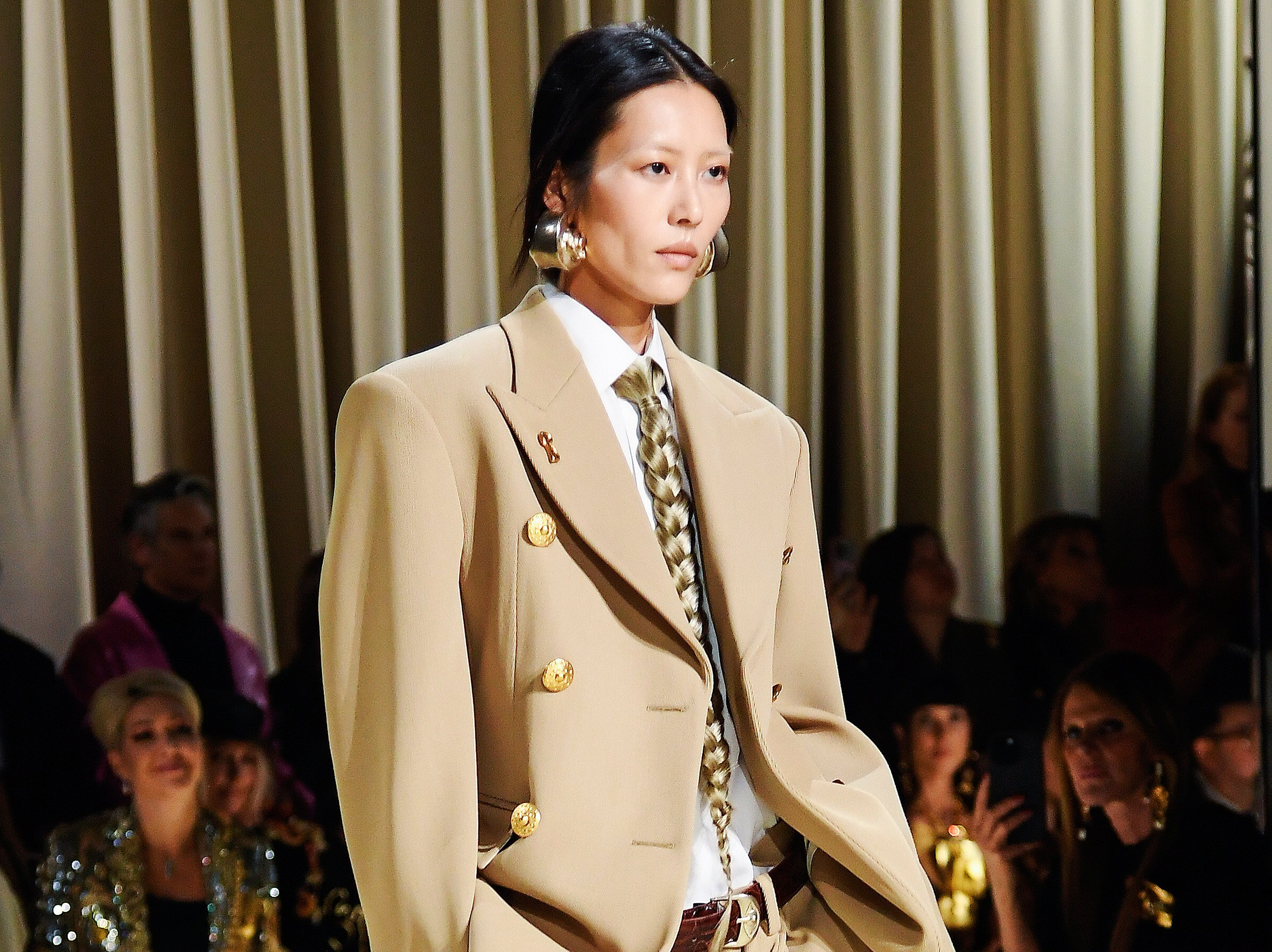 A model wearing a suit with a tie made of braided tie walking down a runway.