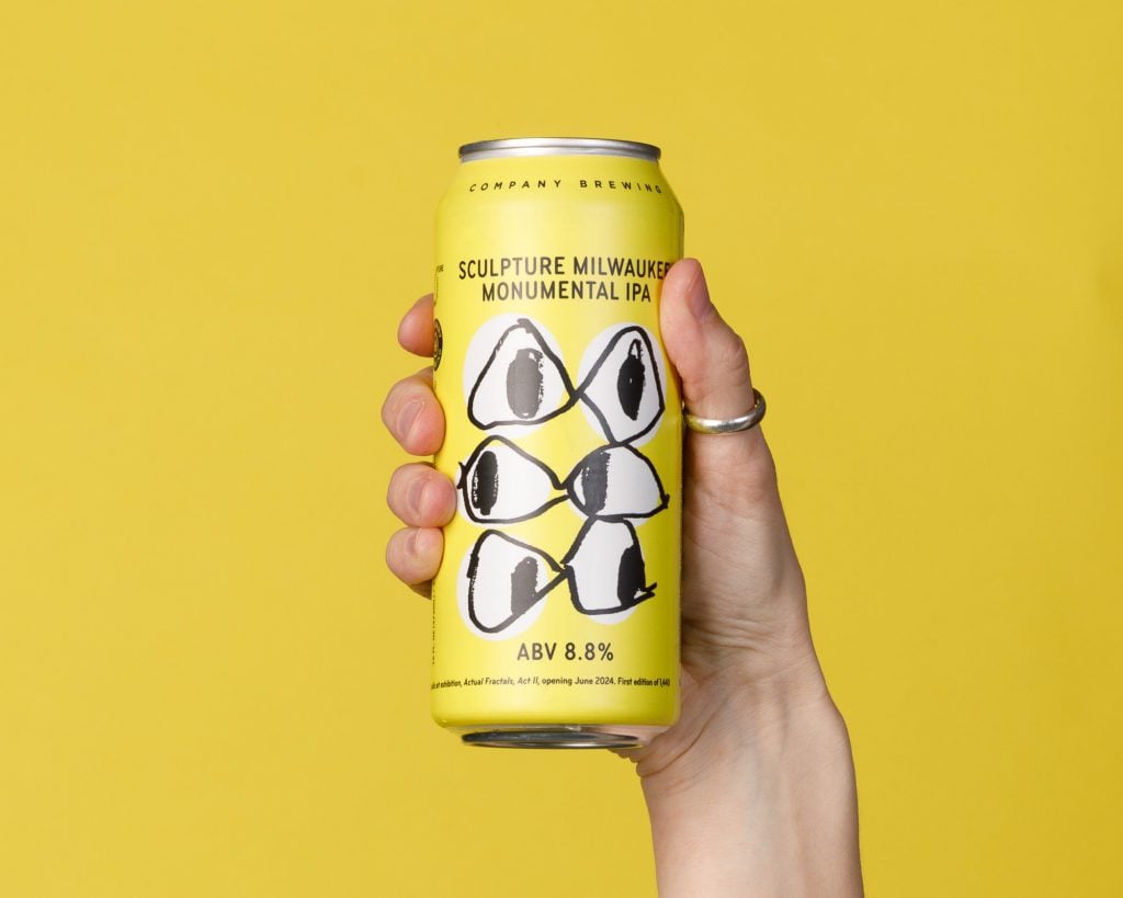 A hand grasping a beer can featuring a design of six eyes on a yellow background