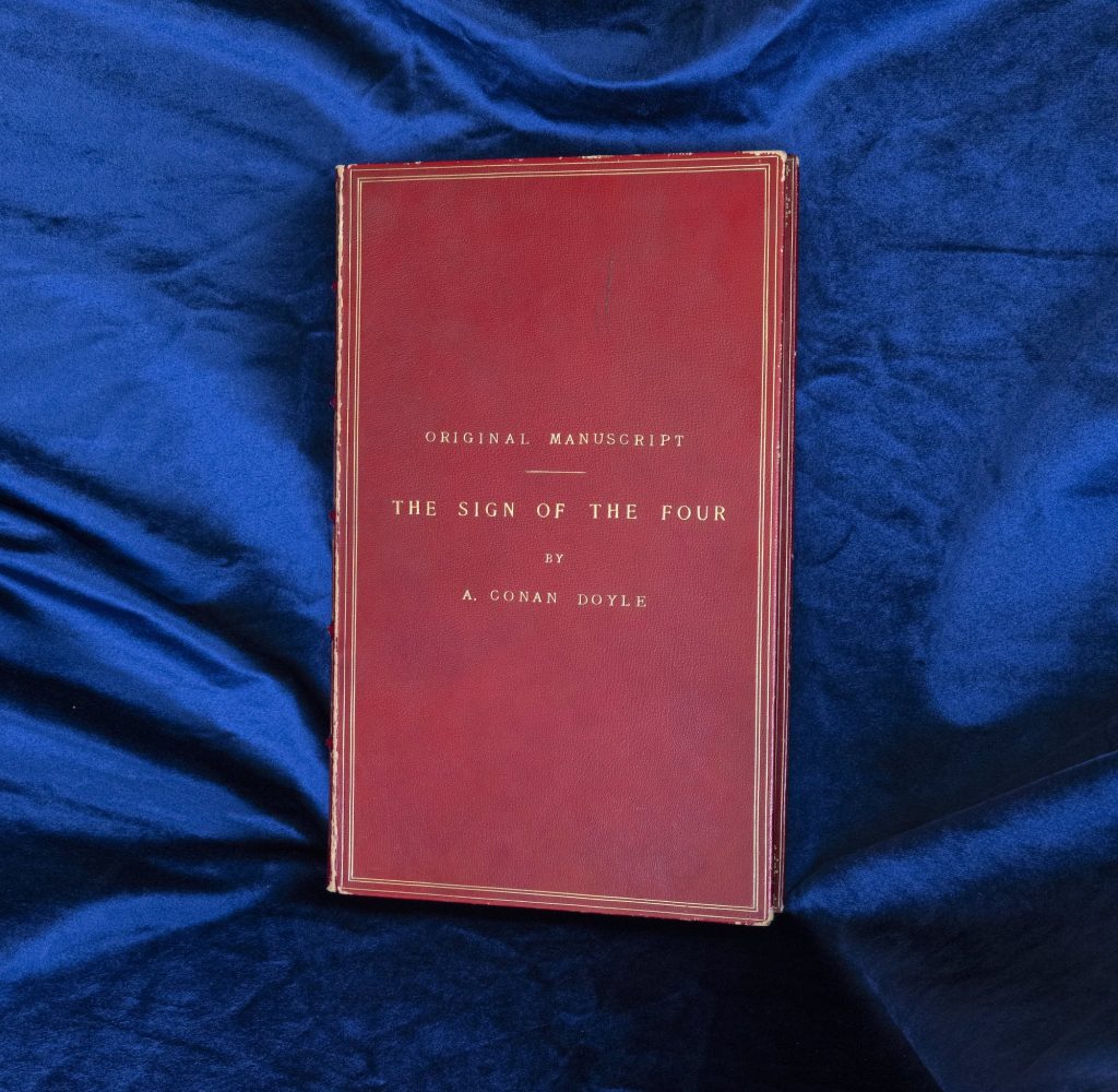 Sir Arthur Conan Doyle's 'The Sign of Four' cover against dark blue fabric.