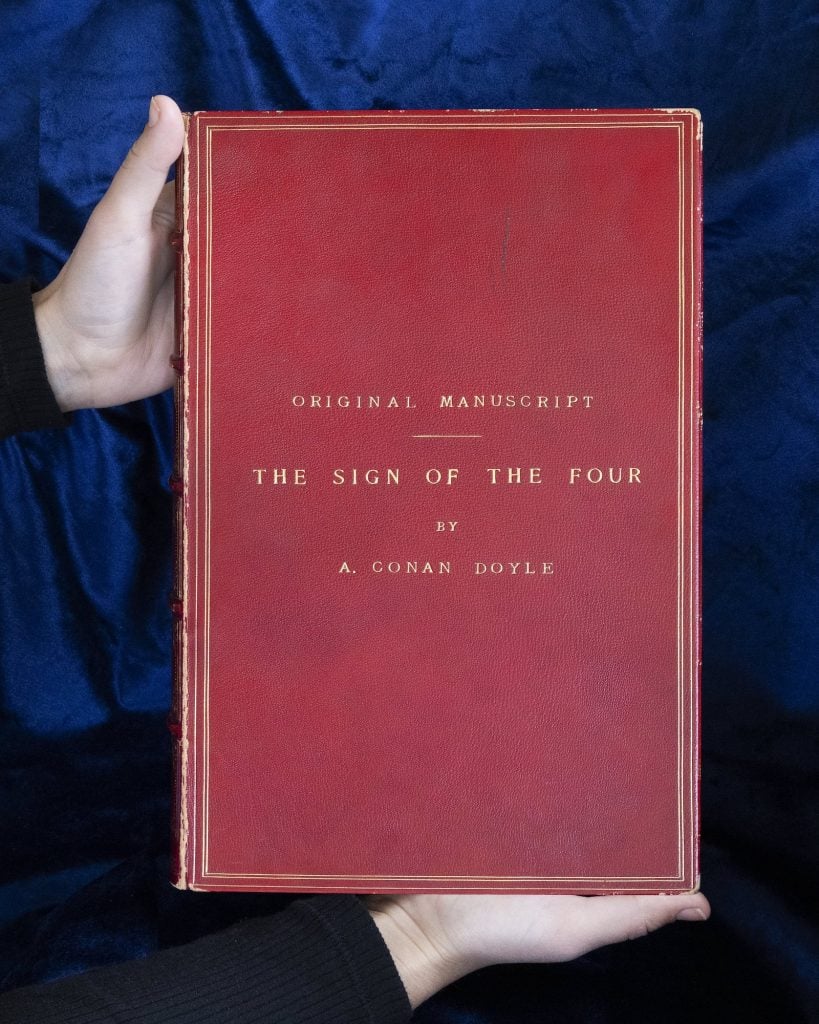 Sir Arthur Conan Doyle's 'The Sign of Four' cover against dark blue fabric.