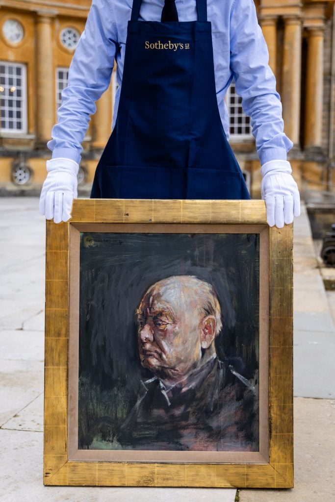 A man wearing a Sotheby's-branded apron holding a framed sketch of Winston Churchill