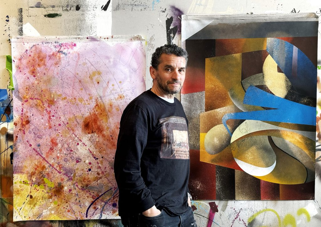 A man, artist Lee Quiñones, standing between two of his artworks-in-progress.