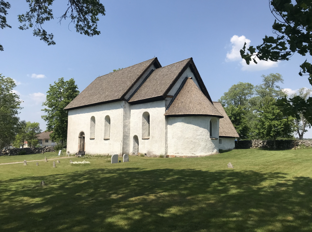 A photograph of a pristine white church on green grass beneath blue skies