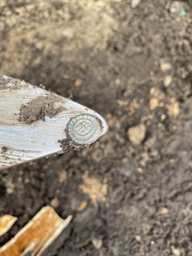 A closeup photo of an old silver coin on a silver tool, with dirt in the background